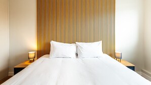 Habitación de hotel con una cama grande, dos mesitas de noche con lámparas y un cabecero de madera con listones.