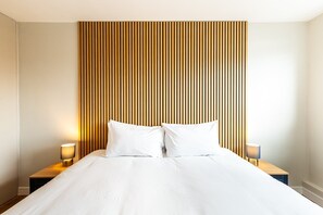 Ein Hotelzimmer mit einem großen Bett, zwei Nachttischen mit Lampen und einem Kopfteil aus Holzleisten.