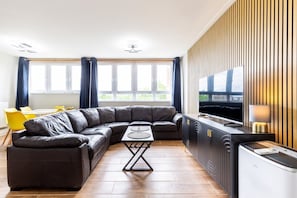 Ein modernes Wohnzimmer mit einem Ecksofa, einem Esstisch und einem Fernseher.