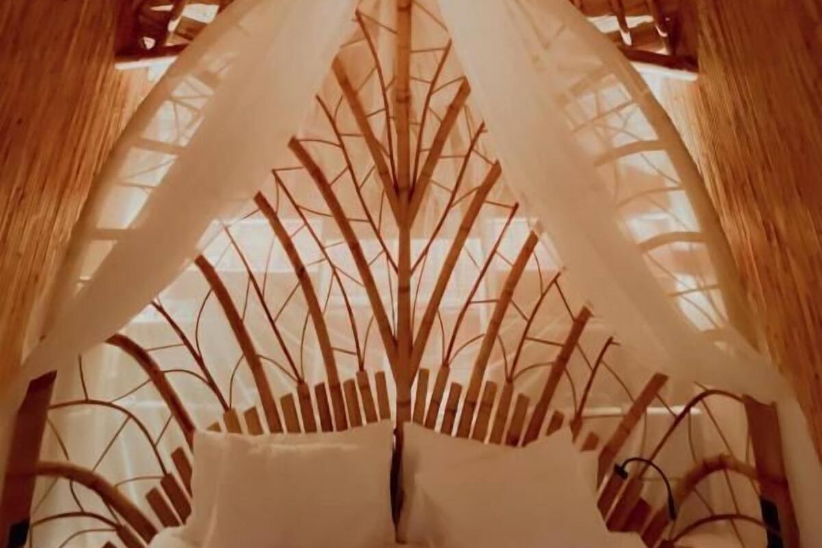 Ein Zimmer mit einem Strohdach, einem Bett mit weißer Bettwäsche und einer hölzernen Struktur, die an einen Baum erinnert.