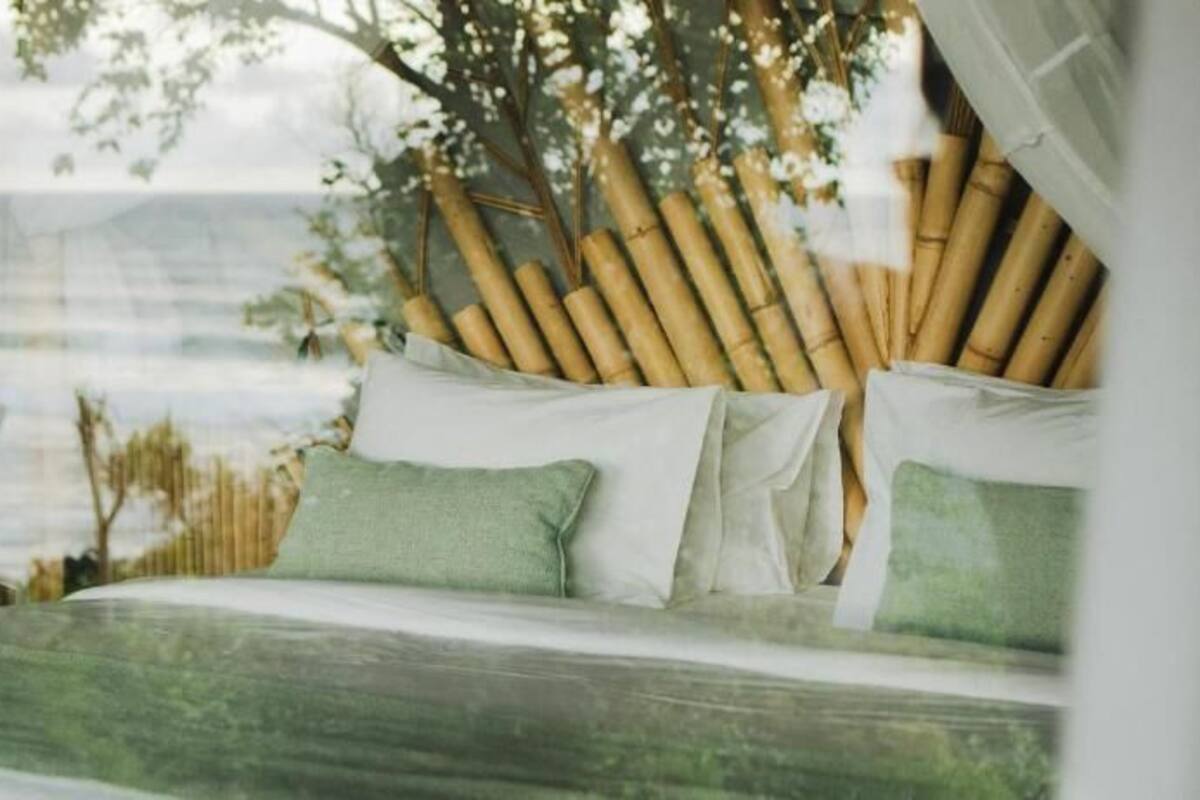 Ein Bett mit Blick auf den Ozean, Bambus-Dekoration und ein weißes Moskitonetz.