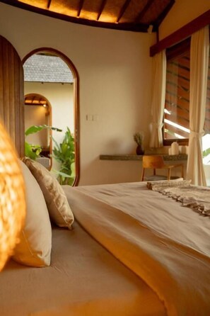 Ein Schlafzimmer mit einem Bett, einem Schreibtisch und einem Stuhl. Ein Fenster mit Vorhängen bietet Blick auf Grünflächen.