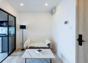 A modern room with a sofa, a coffee table, a floor lamp, and a sliding glass door leading to a kitchen. - チャオプラヤ川の絶景を望む高層階の心地よいお部屋 (Chang Wat Nonthaburi)