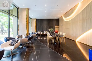 A modern hotel lobby with a long reception desk, seating area with sofas and chairs, and large windows offering a view of the outdoors. - チャオプラヤ川の絶景を望む高層階の心地よいお部屋 (Chang Wat Nonthaburi)
