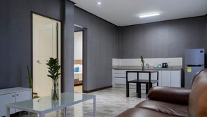 A modern living room with a glass coffee table, a brown leather sofa, and a kitchen area with a refrigerator and a dining table. - Adela Resort Panglao (Panglao)