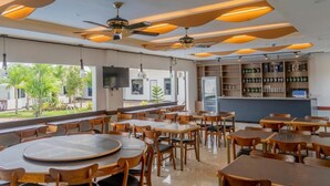 A restaurant with round tables, ceiling fans, and a bar area with shelves of bottles. - Adela Resort Panglao (Panglao)