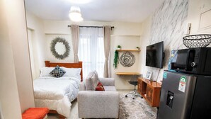 Una camera d'albergo compatta con un letto, un divano, una scrivania, una TV, un frigorifero e un forno a microonde.