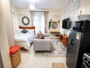 Ein kleines Hotelzimmer mit Bett, einer Sitzecke, einem Schreibtisch, einem Fernseher, einem Kühlschrank und einer Mikrowelle.