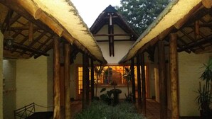 A covered walkway with wooden pillars and a thatched roof, leading to a building with large windows.