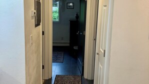 A hallway with a patterned rug, white walls, and a door leading to another room. - The Birch Loft - Woodland Retreat (Anchorage)