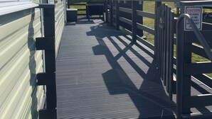 A covered outdoor area with a metal staircase leading to a deck, surrounded by mobile homes. - Cozy Mobile Home at Havens Reighton Sands Holiday Park, Pet-friendly Retreat (Filey)