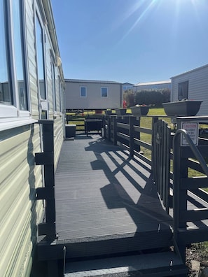 A covered outdoor area with a metal staircase leading to a deck, surrounded by mobile homes. - Cozy Mobile Home at Havens Reighton Sands Holiday Park, Pet-friendly Retreat (Filey)