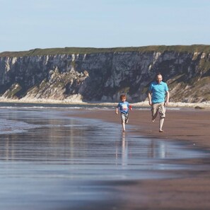 A beach with a person and a child walking on the sand, cliffs in the background. - Cozy Mobile Home at Havens Reighton Sands Holiday Park, Pet-friendly Retreat (Filey)