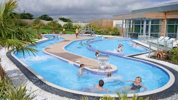 Uma área de piscina com várias piscinas, um elemento aquático e um edifício com grandes janelas.