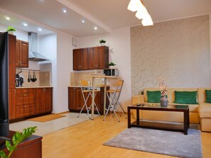 Ein kompakter Wohnbereich mit Küchenzeile, einem Essbereich mit Tisch und Stühlen, einer Couch mit grünen Kissen und einem Couchtisch.