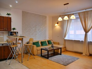 A compact living space with a kitchenette, a sofa with green cushions, a coffee table, and a dining area with chairs. - Designer 1BR Luxury Retreat in Center of Warsaw (Warsaw)