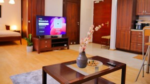 A modern living room with a flat-screen TV, wooden furniture, a vase with flowers, and a dining area. - Designer 1BR Luxury Retreat in Center of Warsaw (Warsaw)