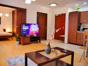 Ein modernes Wohnzimmer mit Flachbildfernseher, Holzmöbeln, einer Vase mit Blumen und einem Essbereich.