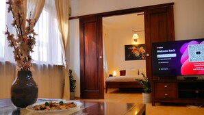 A hotel room with a bed, a TV displaying a welcome screen, a vase with flowers, and a dining table with a plate of food. - Designer 1BR Luxury Retreat in Center of Warsaw (Warsaw)