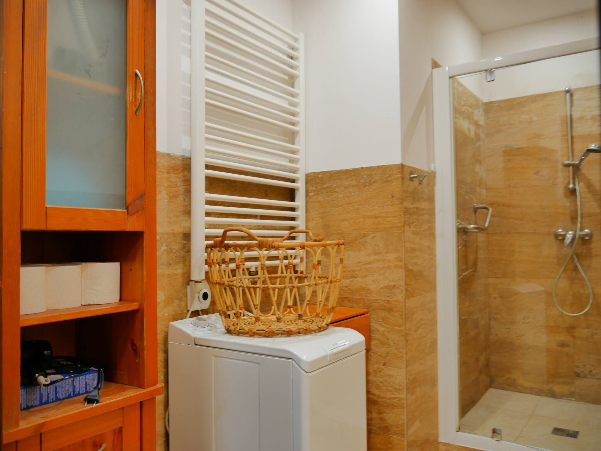 Un baño con lavadora, una cesta de mimbre, toallero y zona de ducha.