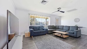 A modern living room with a sectional sofa, a flat-screen TV, a ceiling fan, and a large window.