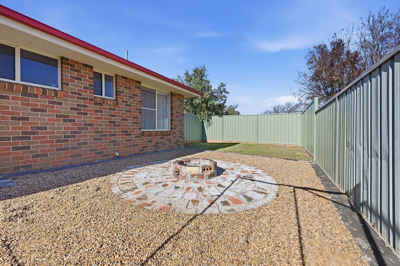 A brick house with a red roof, a circular fire pit, and a metal fence.