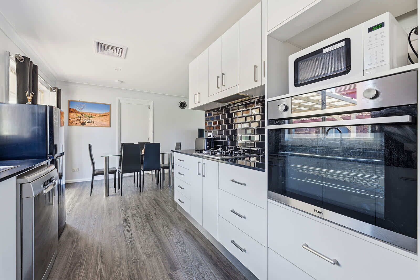 A modern kitchen with white cabinets, a built-in oven, a microwave, and a dining area with a table and chairs.
