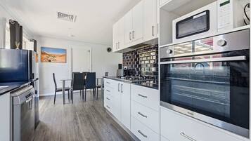A modern kitchen with white cabinets, a built-in oven, a microwave, and a dining area with a table and chairs.