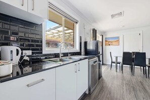 A modern kitchen with a window, a dining area with chairs, and a view of a desert landscape. - Canterbury House - Firepit Retreat Near Mall (Dubbo)