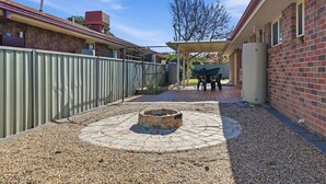 Ein Garten mit Feuerstelle, überdachter Terrasse und einer Ziegelmauer.