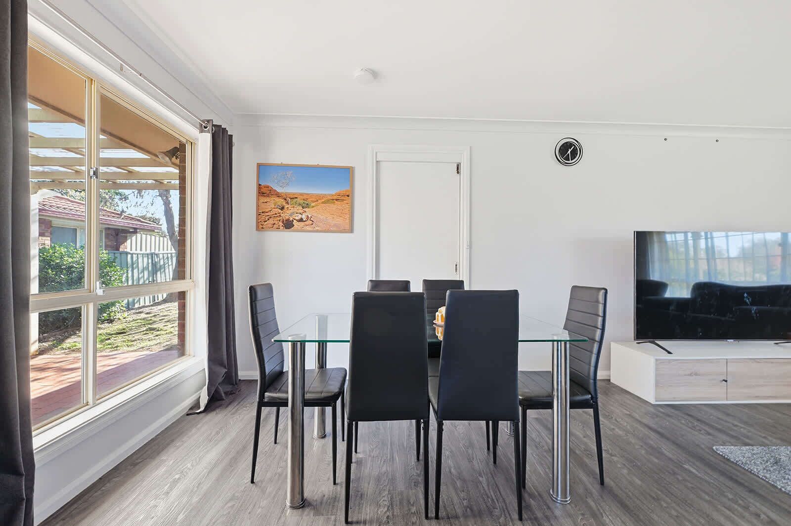 Un salon moderne avec une table à manger en verre, des chaises noires, un téléviseur à écran plat et un tableau accroché au mur.