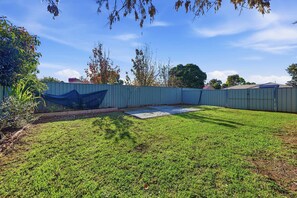 Un pati amb una zona tancada per una tanca, una zona de formigó i un prat.
