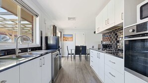 Eine moderne Küche mit weißen Schränken, Edelstahlgeräten und einem Essbereich mit Tisch und Stühlen.