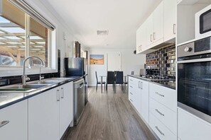Una cuina moderna amb armaris blancs, electrodomèstics d'acer inoxidable i una zona de menjador amb taula i cadires.
