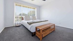 A bedroom with a bed, a wooden bench, a ceiling fan, and a window with curtains.