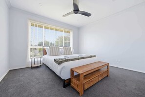 A bedroom with a bed, a wooden bench, a ceiling fan, and a window with curtains.