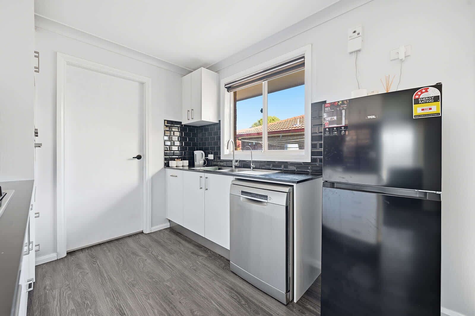 A modern kitchen with white cabinets, a black countertop, a stainless steel dishwasher, and a refrigerator.