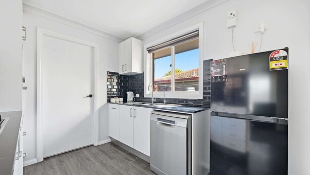 A modern kitchen with white cabinets, a black countertop, a stainless steel dishwasher, and a refrigerator.