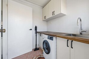A compact kitchen with a washing machine, a sink, and a door. - Canterbury House - Firepit Retreat Near Mall (Dubbo)