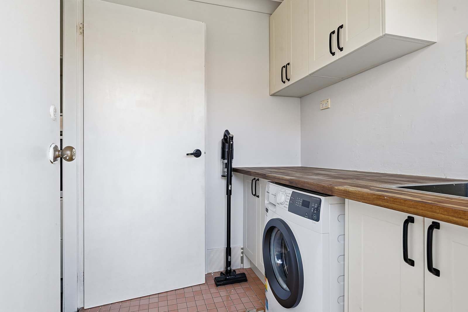 A compact laundry room with a washing machine, a drying rack, and a door with a handle.