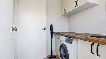 A compact laundry room with a washing machine, a drying rack, and a door with a handle.