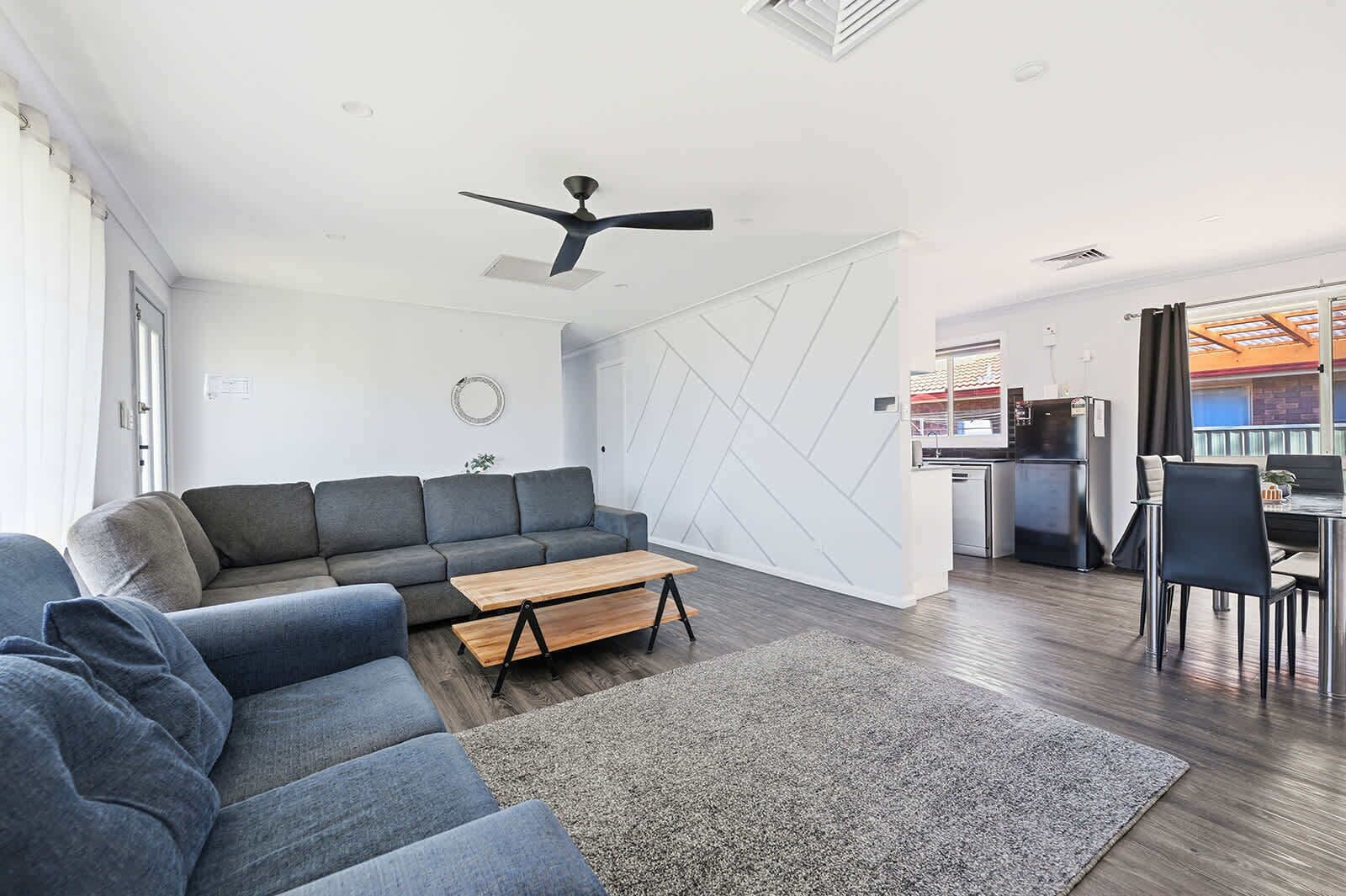 Una sala de estar moderna con un sofá seccional gris, una mesa de centro de madera y un ventilador de techo.