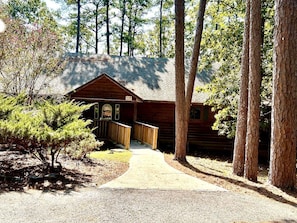 A log cabin with a porch, a pathway leading to it, and surrounding trees. - Amazing Cabin with Fireplace, Barbecue and Tennis Court in Mount Ida, Arkansas (Mount Ida)