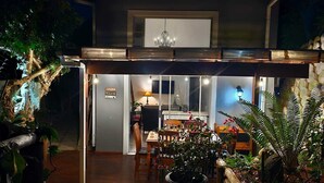 Ein Haus mit einer überdachten Terrasse, einem Essbereich und einer durch die offene Tür einsehbaren Küche.