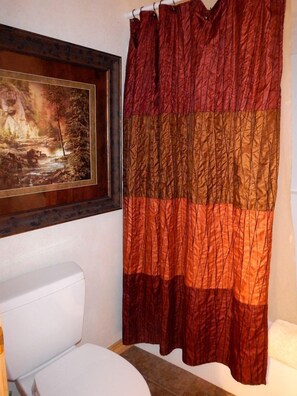 Een badkamer met een wit toilet, een ingelijst schilderij aan de muur en een douchegordijn met rode en bruine strepen.