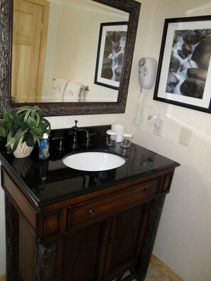 A bathroom with a black countertop sink, a mirror, a hairdryer, and a framed picture on the wall. - Chic Lakefront Cottage with Hot-Tub Perfect for Water Activities in Mount Ida, Arkansas (Mount Ida)