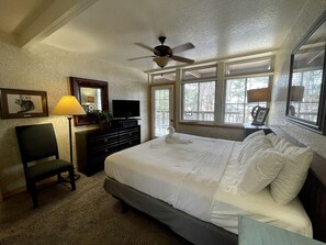 Ein Schlafzimmer mit Bett, Schreibtisch, Stuhl, Fernseher und Deckenventilator.