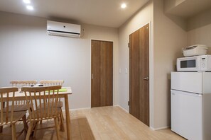 A small kitchen with a microwave and a refrigerator, wooden chairs around a table, and a wooden door. - Star house (Osaka)