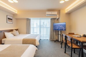 Ein Hotelzimmer mit zwei Betten, einem Fernseher, einem Schreibtisch mit Stühlen und einer Klimaanlage.