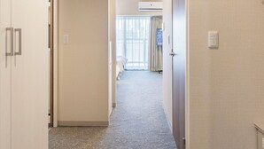 Et hotel med et tæppet gulv, en dør til venstre og et vindue med gardiner i baggrunden.